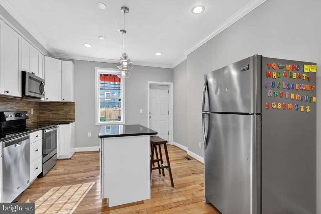 Kitchen with white cabinets, stainless steel appliances, a black-topped island, and hardwood floors.