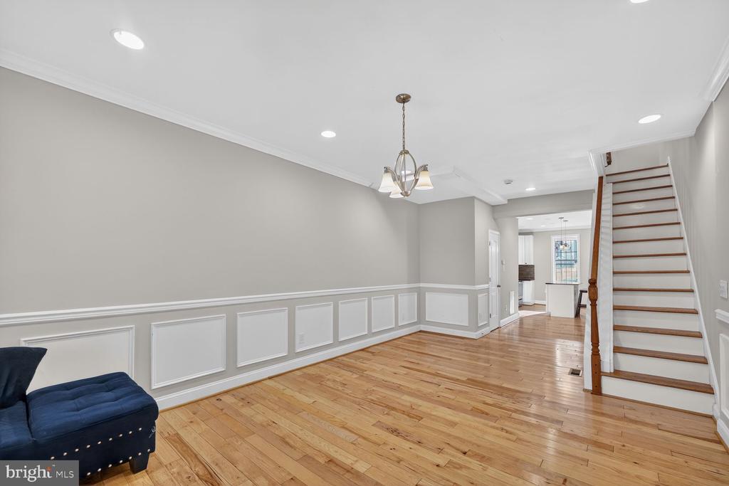 Living area with hardwood floors, white wainscoting, and a staircase beside the kitchen.