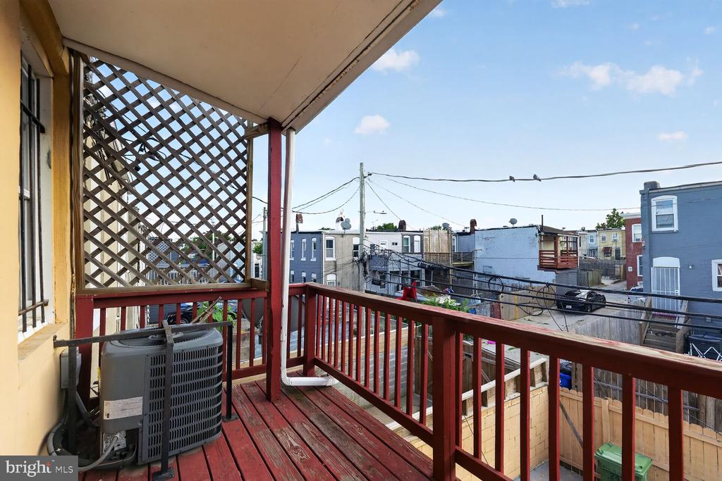 Covered rear deck with red railings and lattice screen overlooking Baltimore rowhouses.
