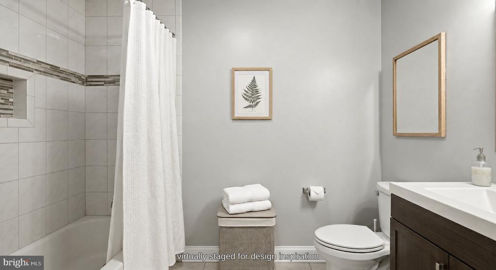 Bathroom with a tiled tub and shower, white curtain, toilet, and dark wood vanity.