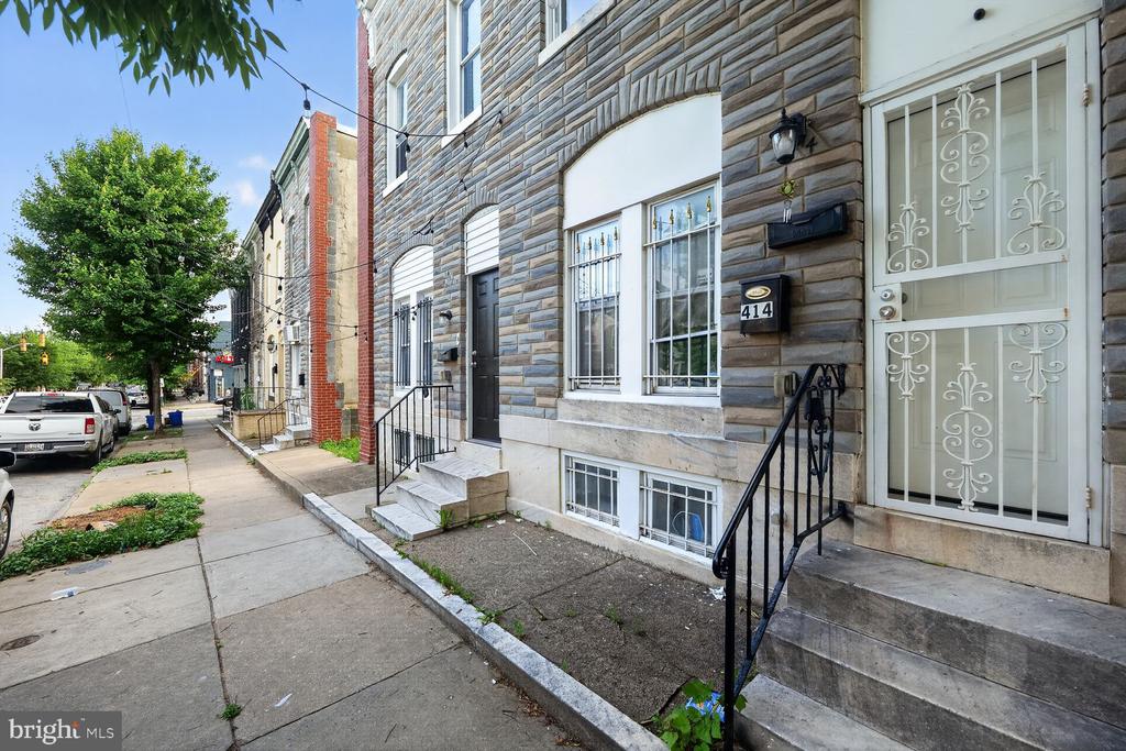 Baltimore rowhouse with a stone facade, ornate security door, and concrete stoop.