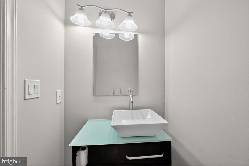 Bathroom vanity with a white vessel sink, pale aqua glass countertop, and dark cabinet.