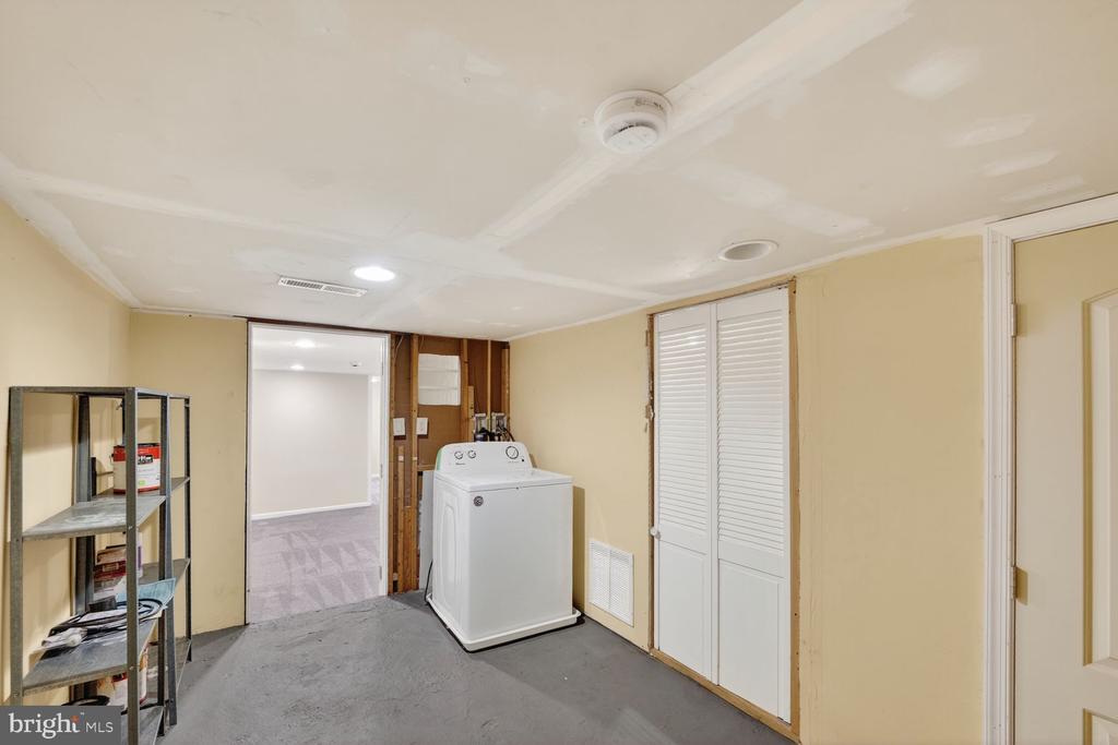 Laundry room with a top-loading washer, metal shelves, and louvered closet doors.