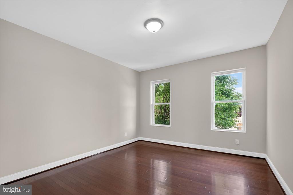 Empty room with dark hardwood floors, neutral walls, and two windows overlooking greenery.