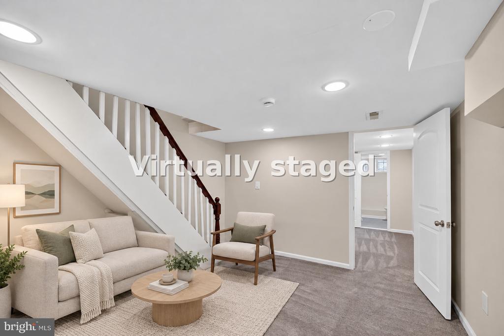 Virtually staged basement living room with a sofa, armchair, and staircase.