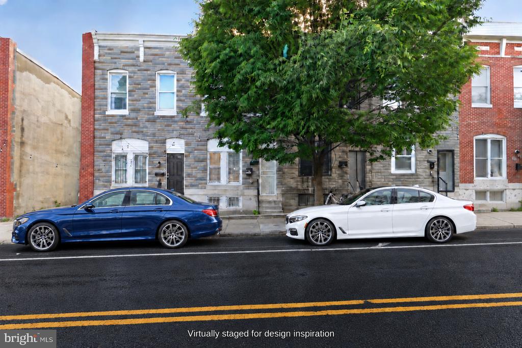 Stone-front Baltimore rowhouses behind a leafy street tree, with two cars parked at the curb.