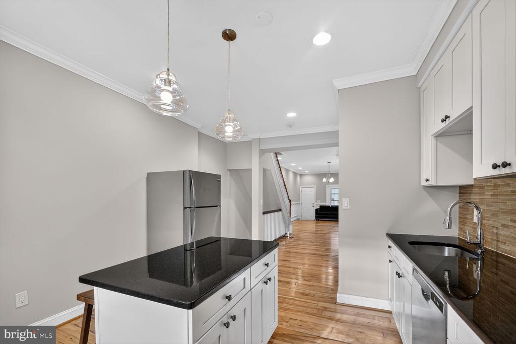 Kitchen with a black-countertop island, white cabinetry, glass pendant lights, and hardwood floors leading to an open living area.