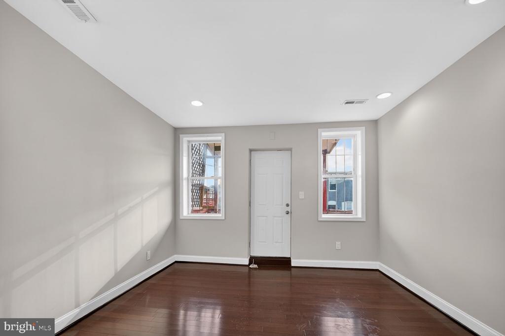Empty room with dark hardwood floors, two windows, and a white exterior door.