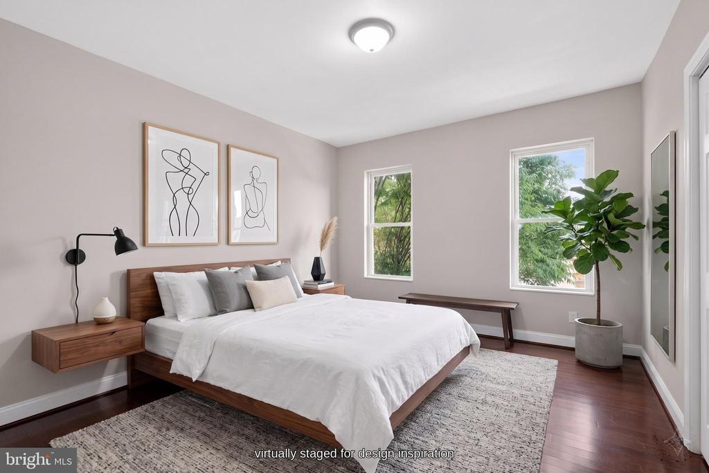 Bedroom with a white bed, wood furnishings, framed line art, and a large potted plant by the windows.