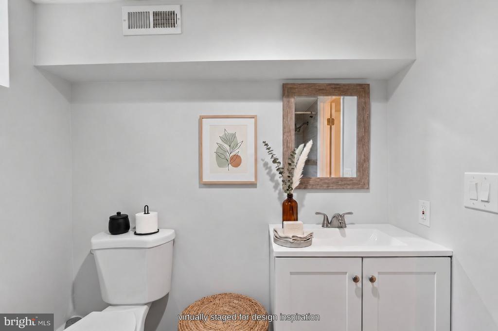 Virtually staged bathroom with a white vanity, framed mirror, and toilet.