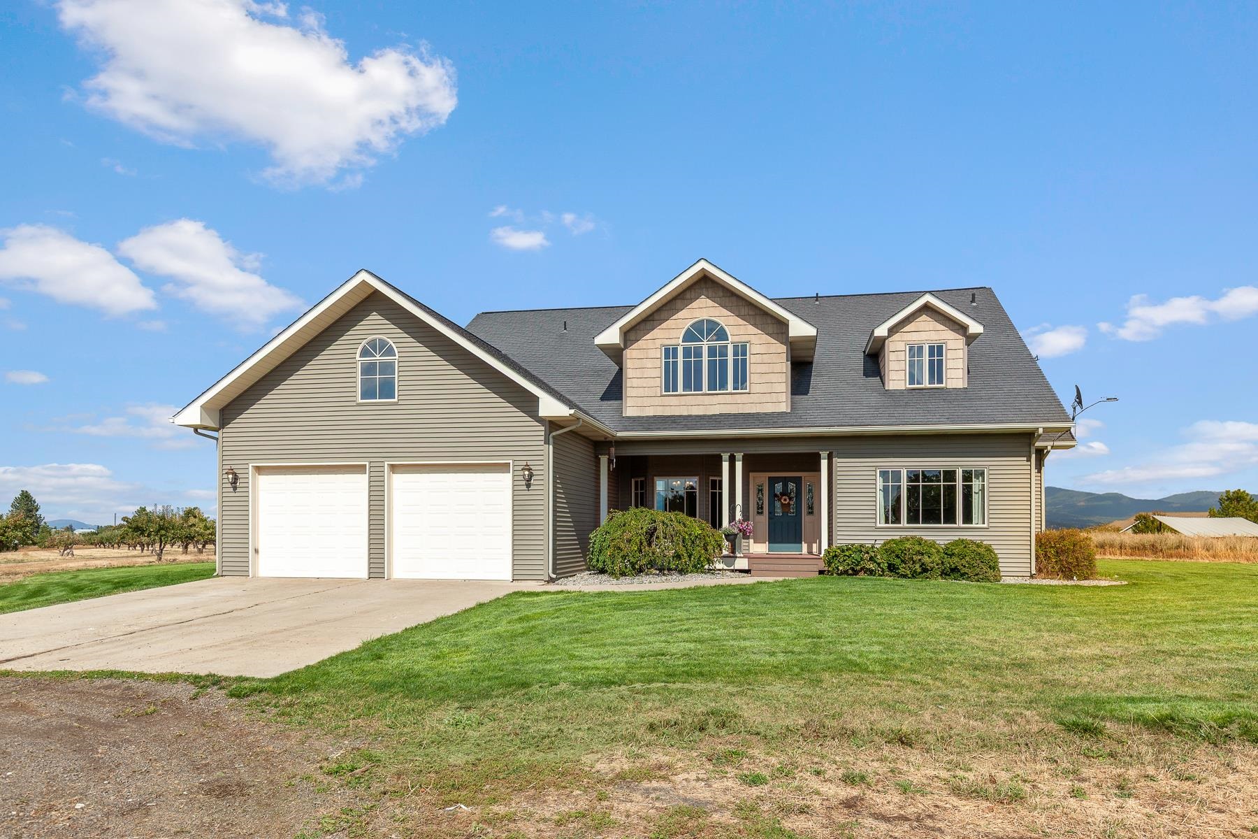 Gray two-story home with a covered porch, double garage, and broad lawn.