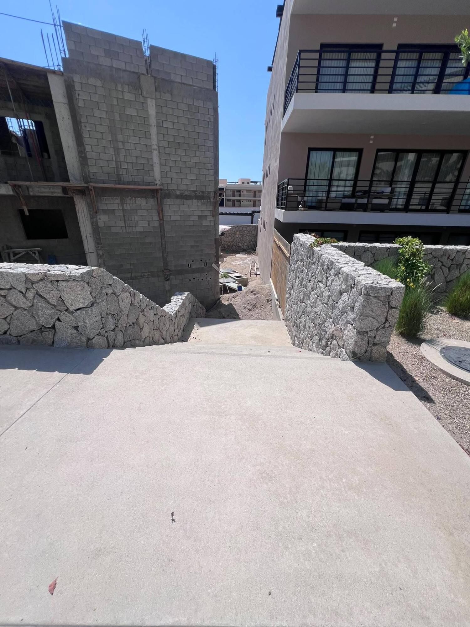 Condominium walkway between stone walls, beside a finished balcony building and unfinished structure.