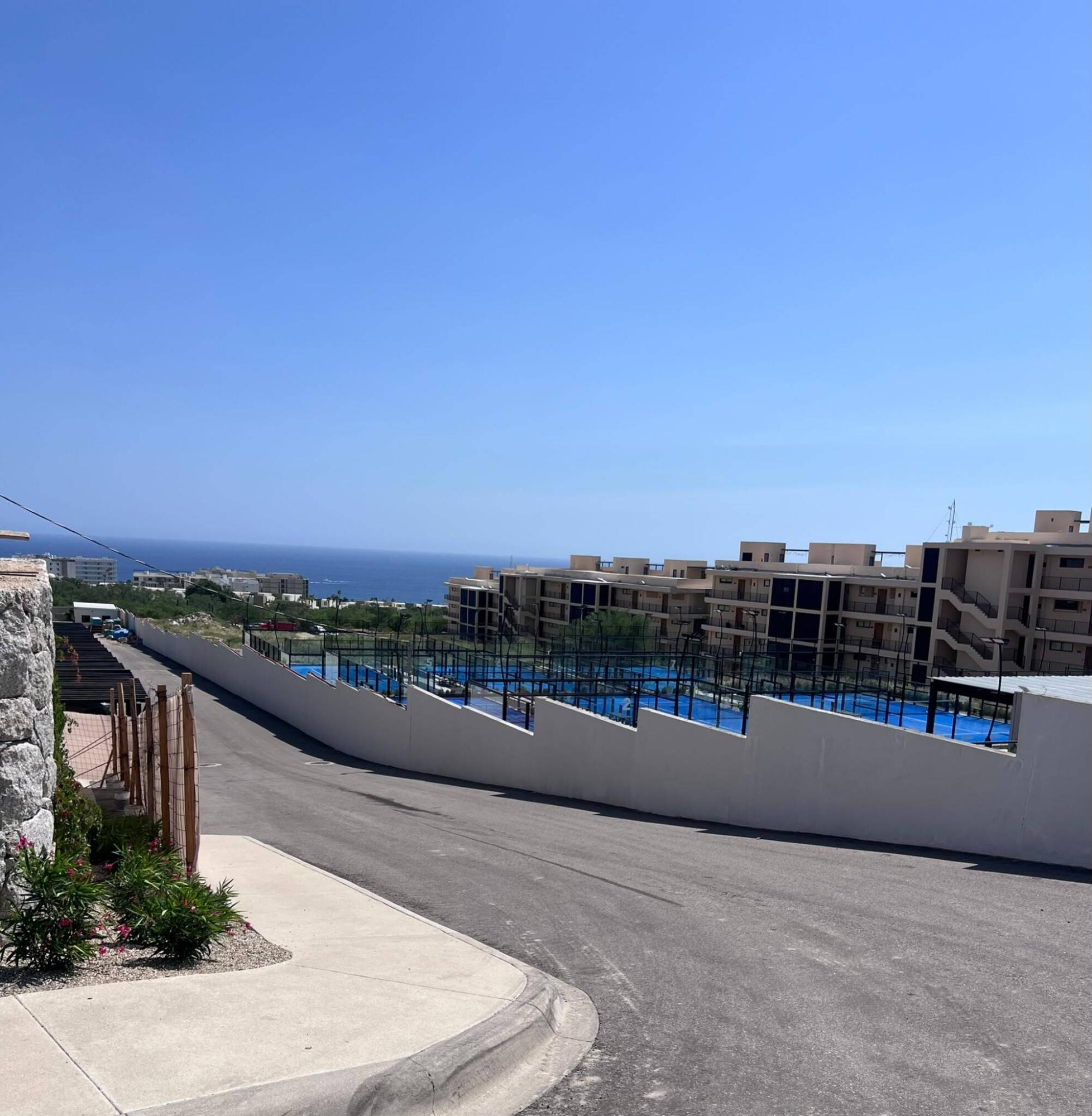 Condominium complex with blue padel courts and ocean visible beyond the buildings.