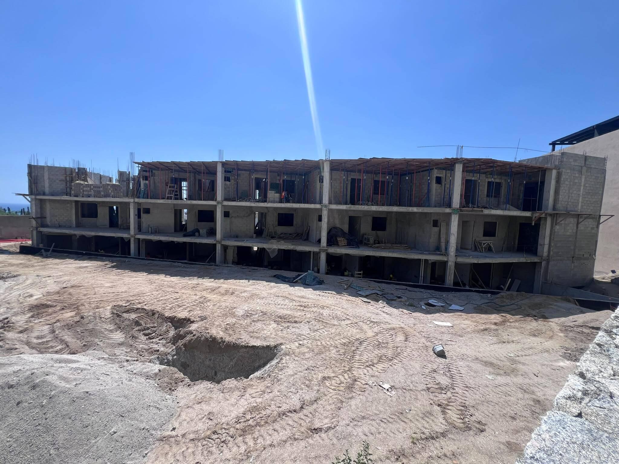Unfinished multi-story concrete building with open facade and construction supports above a dirt site.