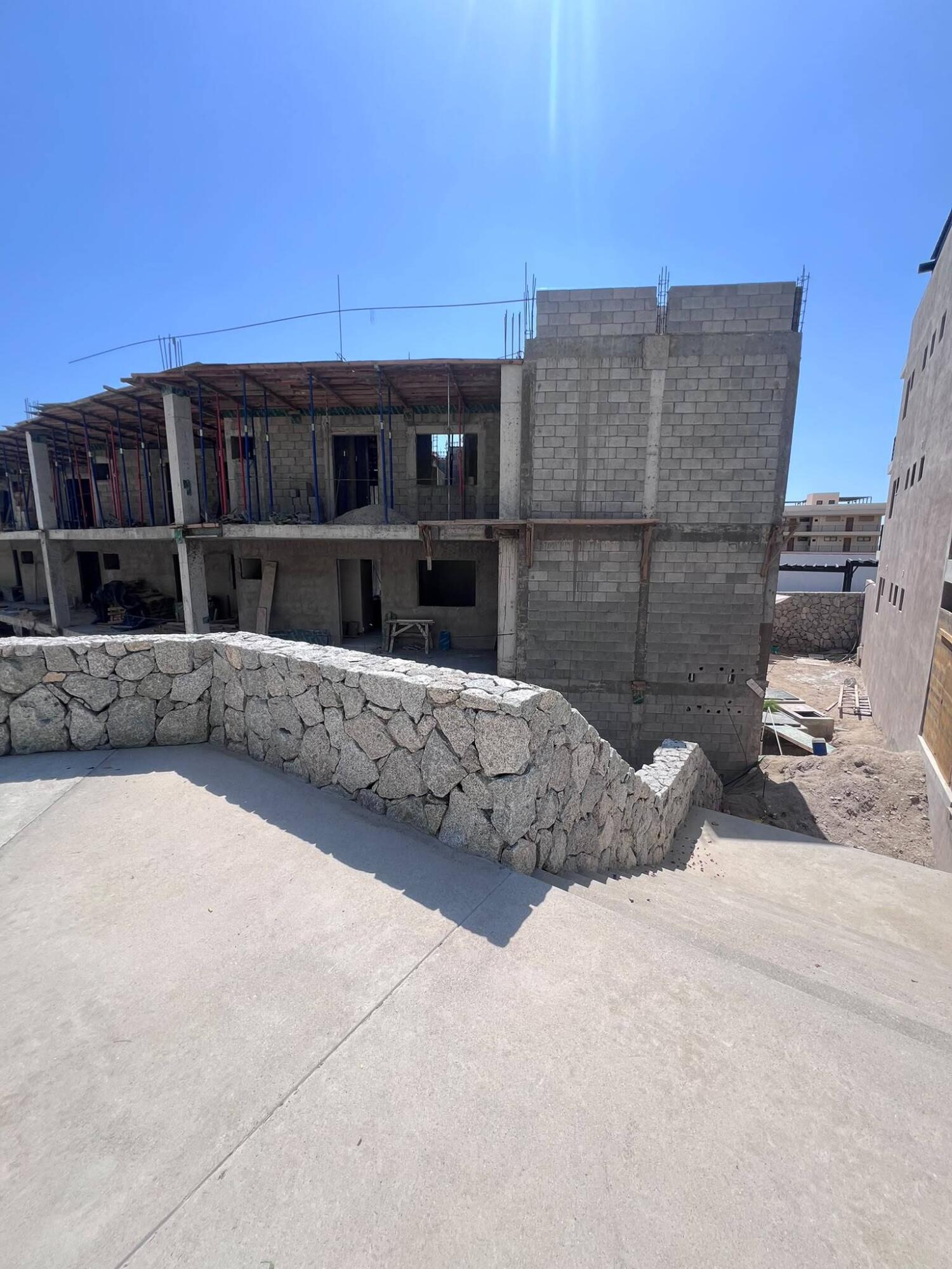 Unfinished multi-story building with exposed framing behind a curved stone retaining wall.