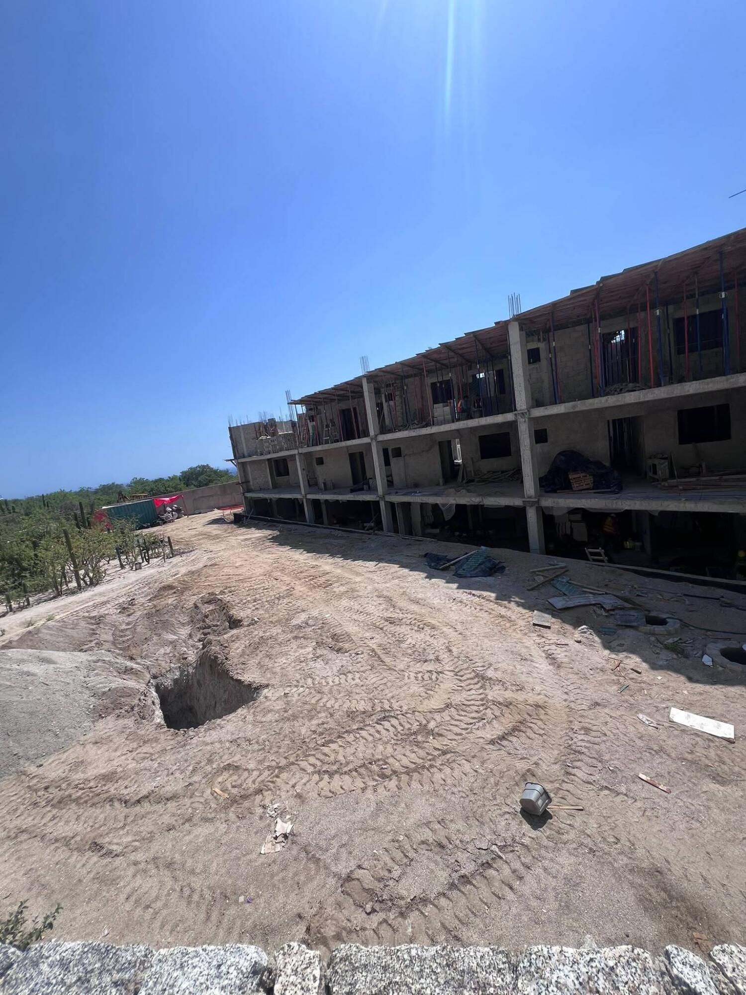 Concrete residential building under construction beside a rutted dirt construction yard.