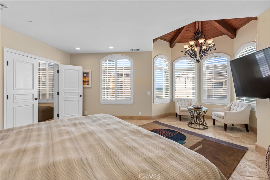 Bedroom with a large bed, arched shuttered windows, vaulted wood ceiling, and sitting area.