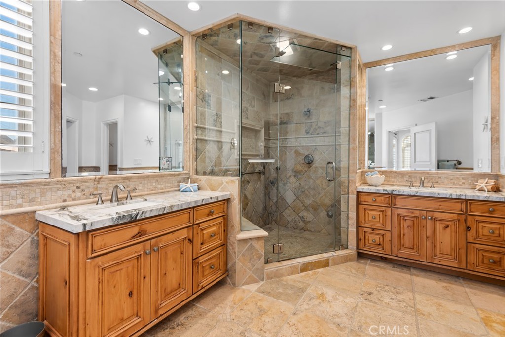 Bathroom with a glass-enclosed stone shower and two wood vanities with marble countertops.