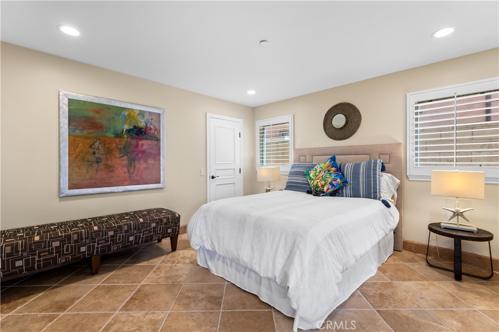 Furnished bedroom with a white bed, colorful accent pillow, shuttered windows, and abstract wall art.
