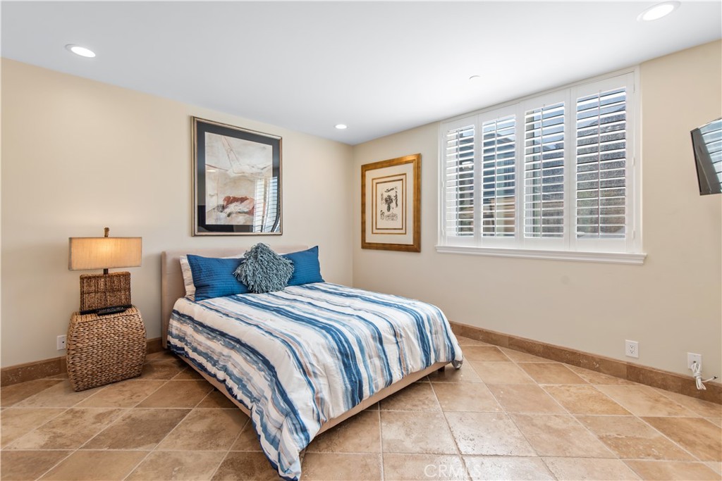 Bedroom with blue-and-white striped bedding, tan tile floor, and plantation shutters.