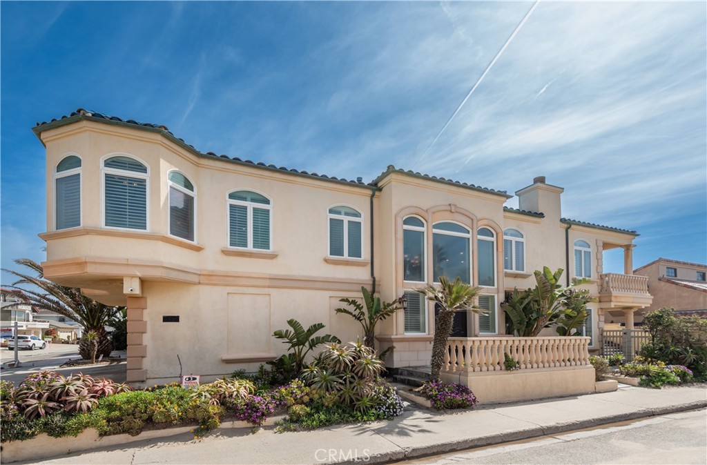 Two-story cream home with arched windows, a tiled roof, and landscaped flower beds.