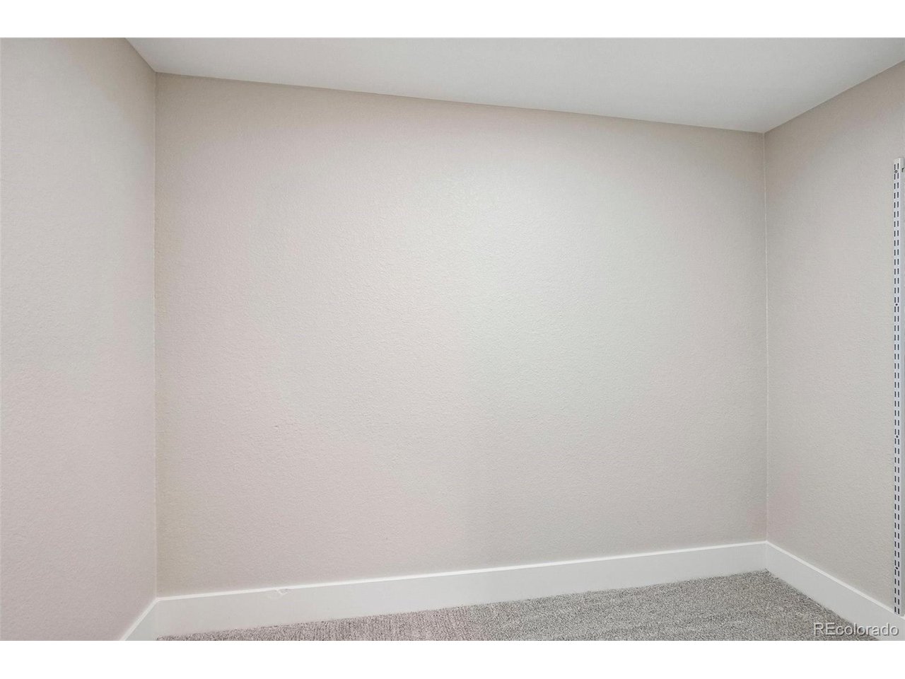 Empty carpeted closet corner with pale walls and a shelving track.
