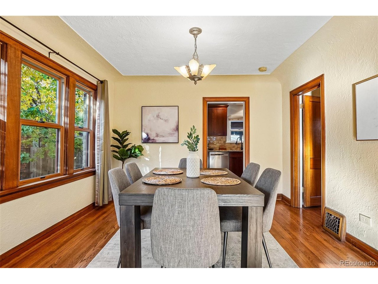 Dining room with a dark table, gray chairs, hardwood floors, and large wood-trimmed windows.