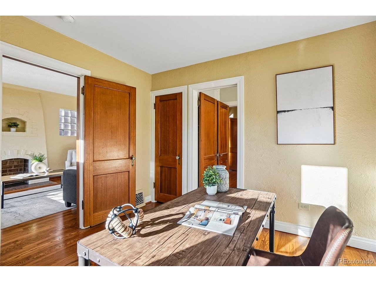Furnished home office with a rustic wood desk, multiple wooden doors, and yellow walls.