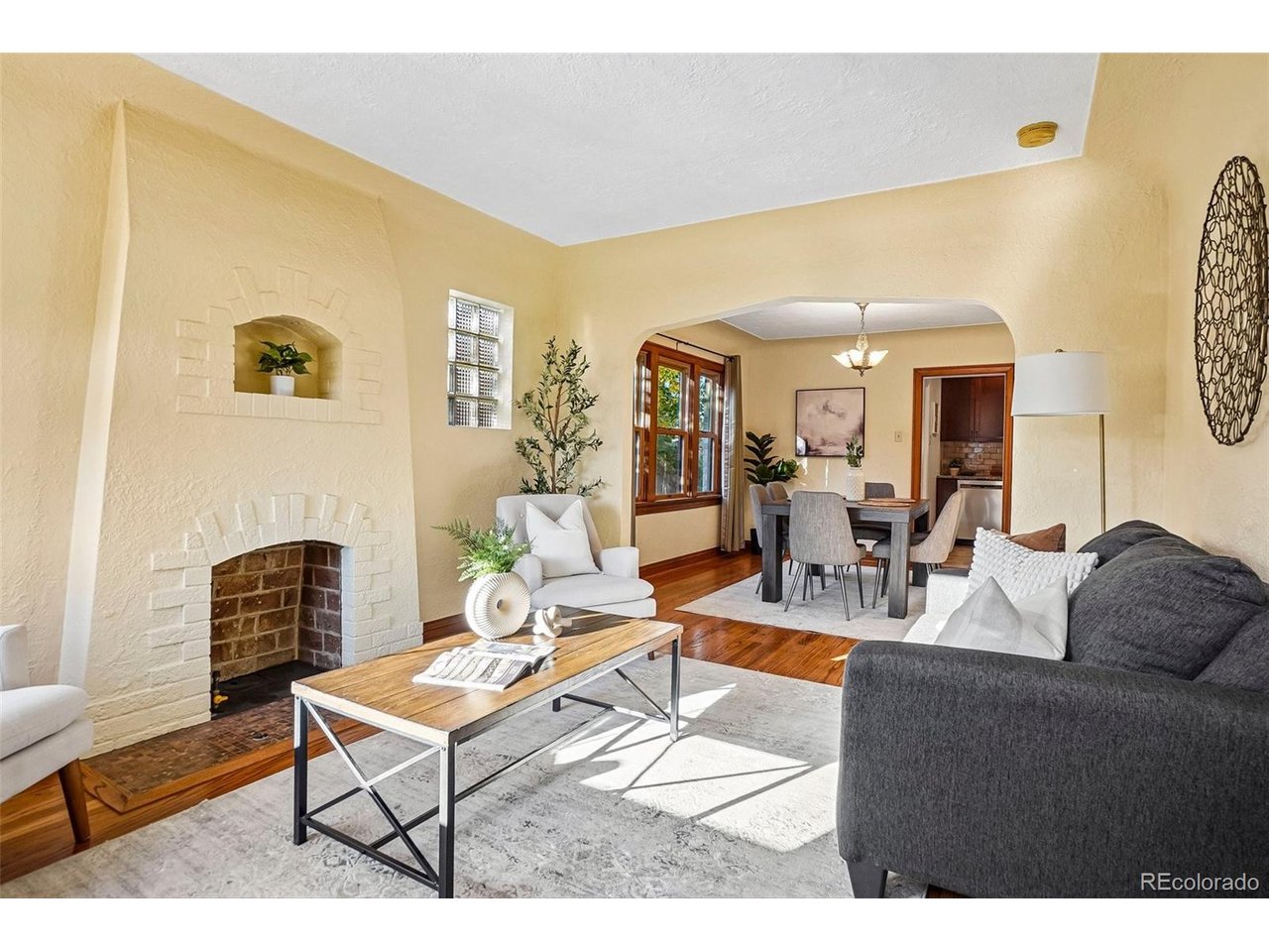 Living room with a white brick fireplace, dark gray sofa, and arched opening to the dining area.