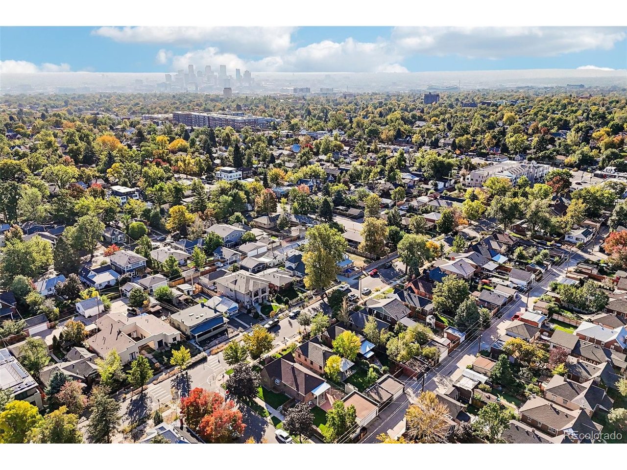 Aerial view of a tree-lined Denver neighborhood with downtown skyline in the distance.
