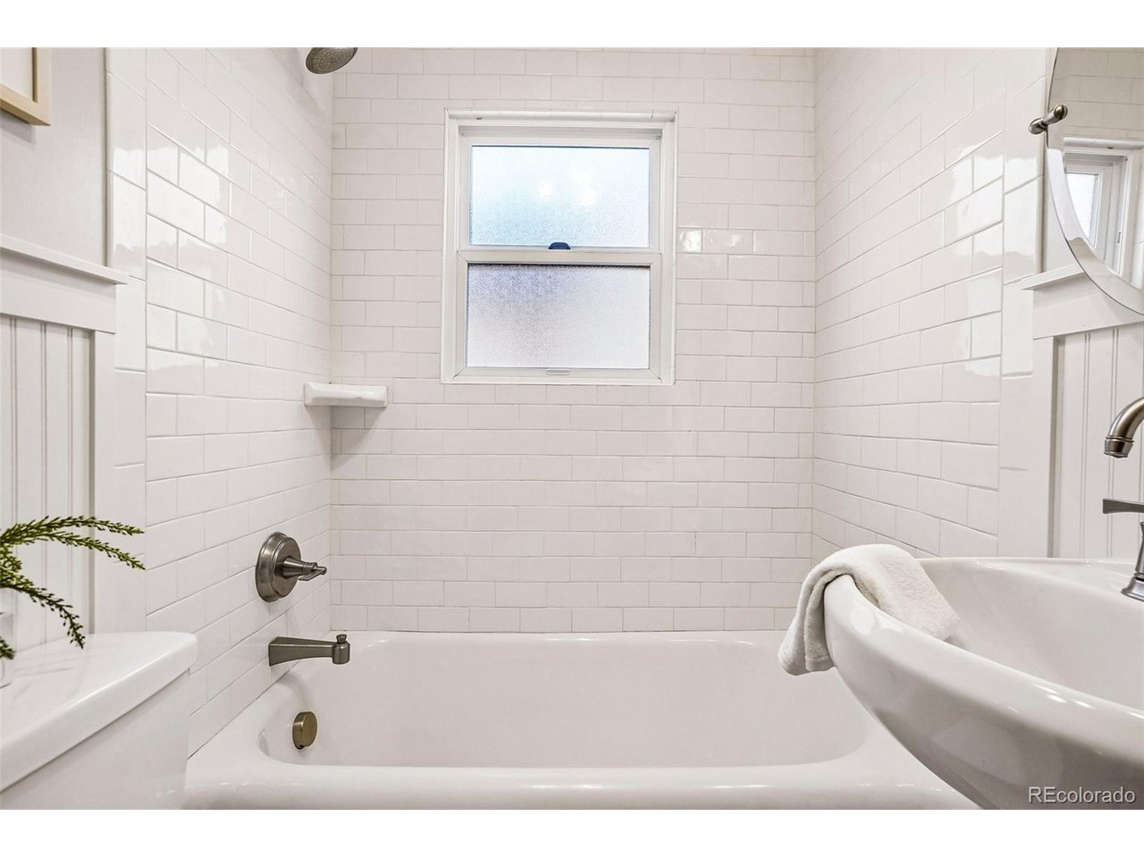 Bathroom with a white subway-tile tub surround, frosted window, and chrome fixtures.