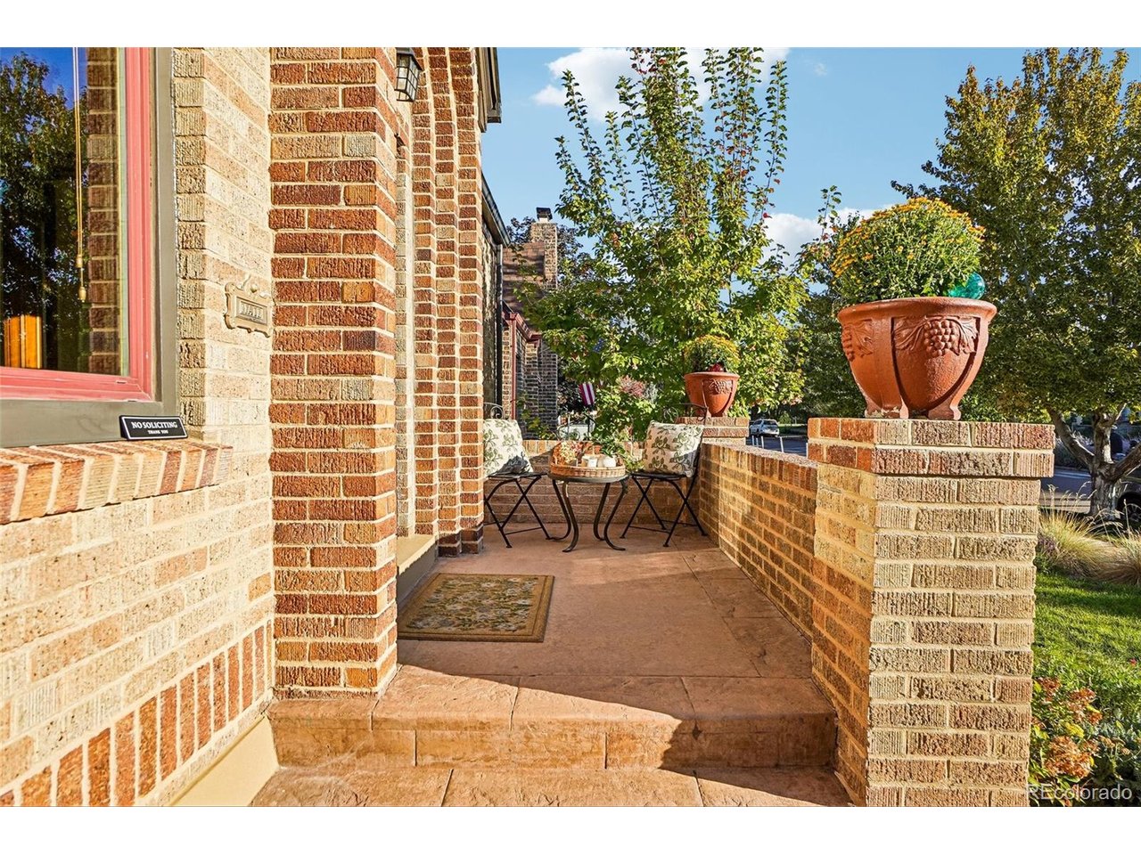 Brick home entrance with a raised porch, outdoor seating, and large terracotta planters.