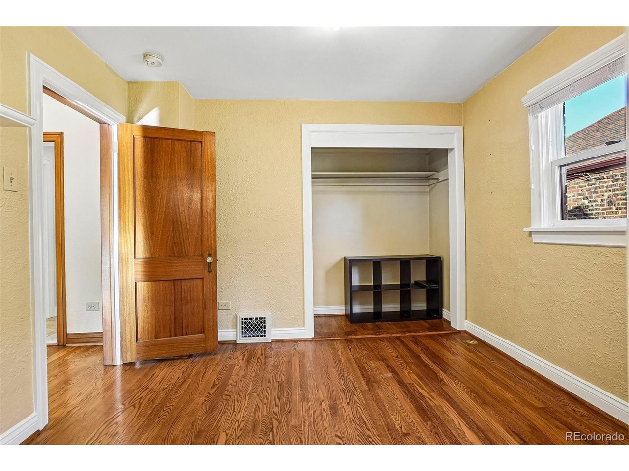 Bedroom with hardwood floors, yellow walls, and an open closet.