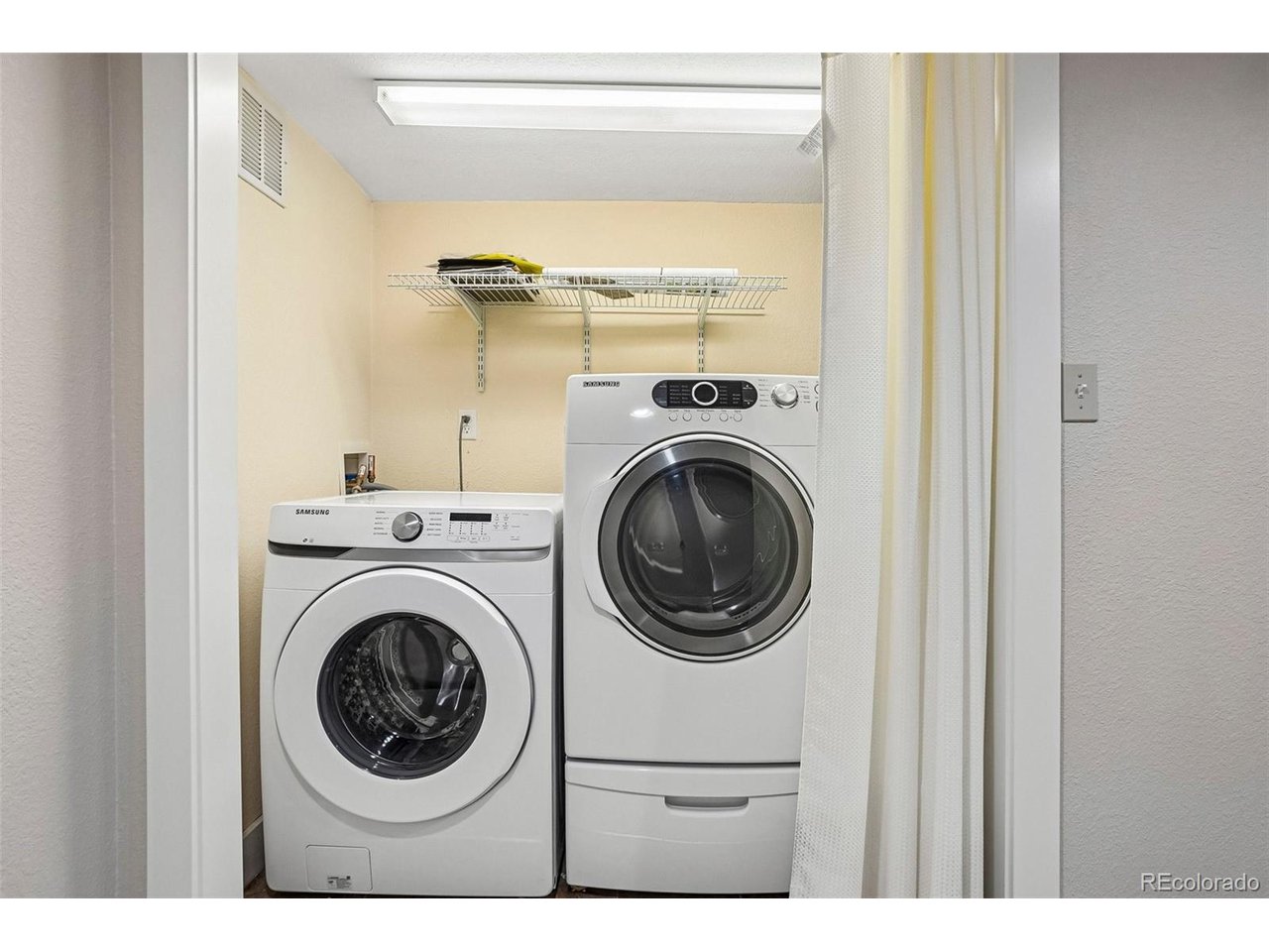 Laundry room with a front-loading washer and dryer beneath a wire storage shelf.