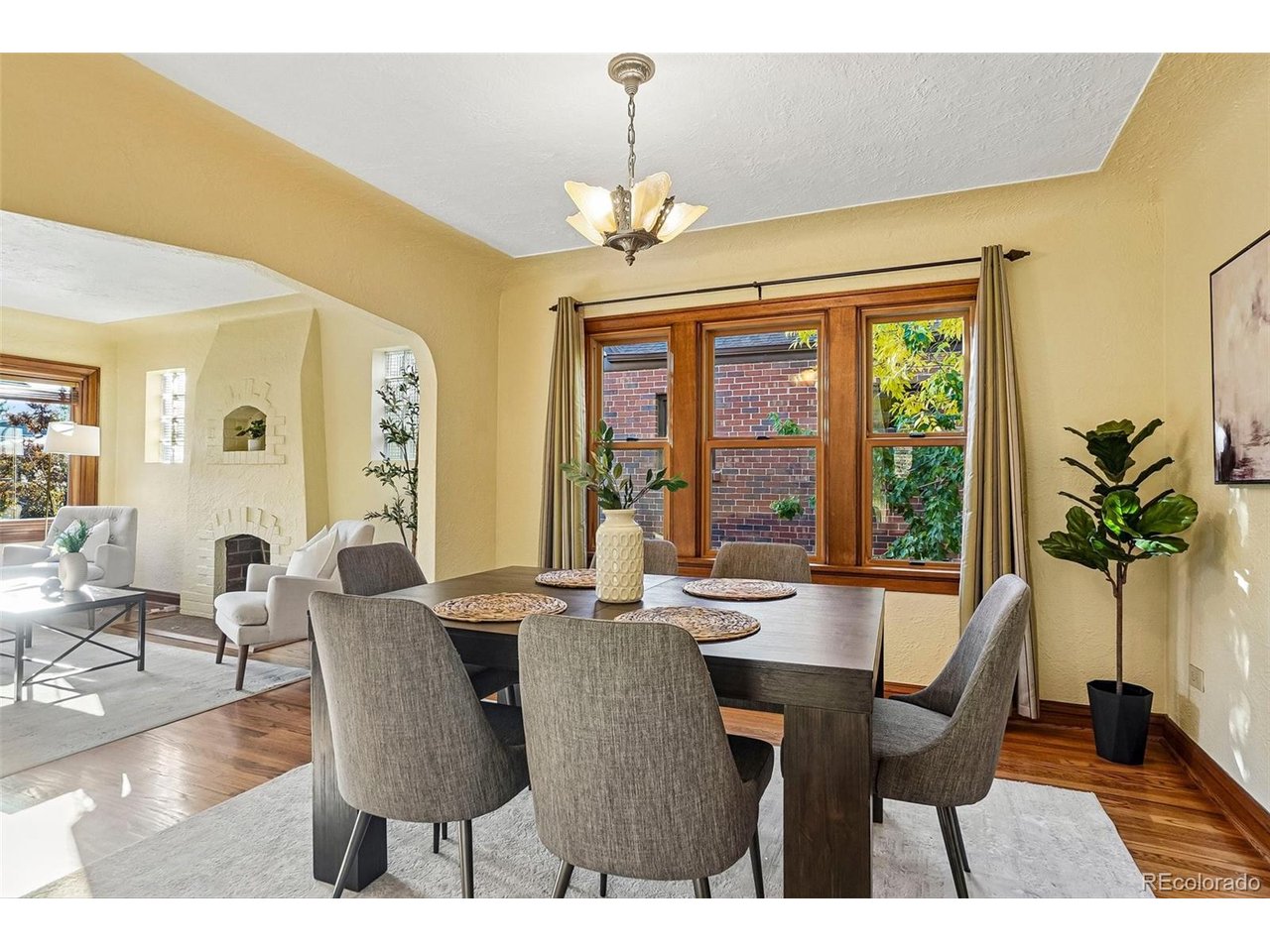 Staged dining room with wood-framed windows, gray upholstered chairs, and an adjoining living area.