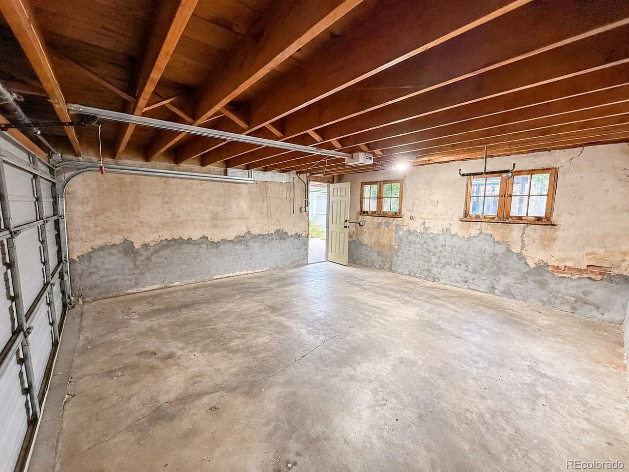 Empty garage with exposed wooden rafters, unfinished walls, and a concrete floor.