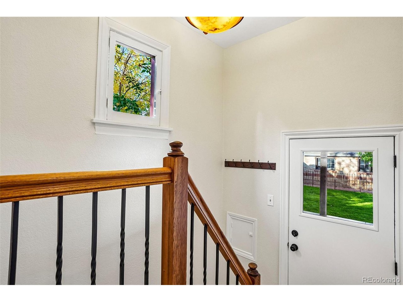 Stair landing with a polished wood railing and a windowed entry door overlooking a fenced yard.