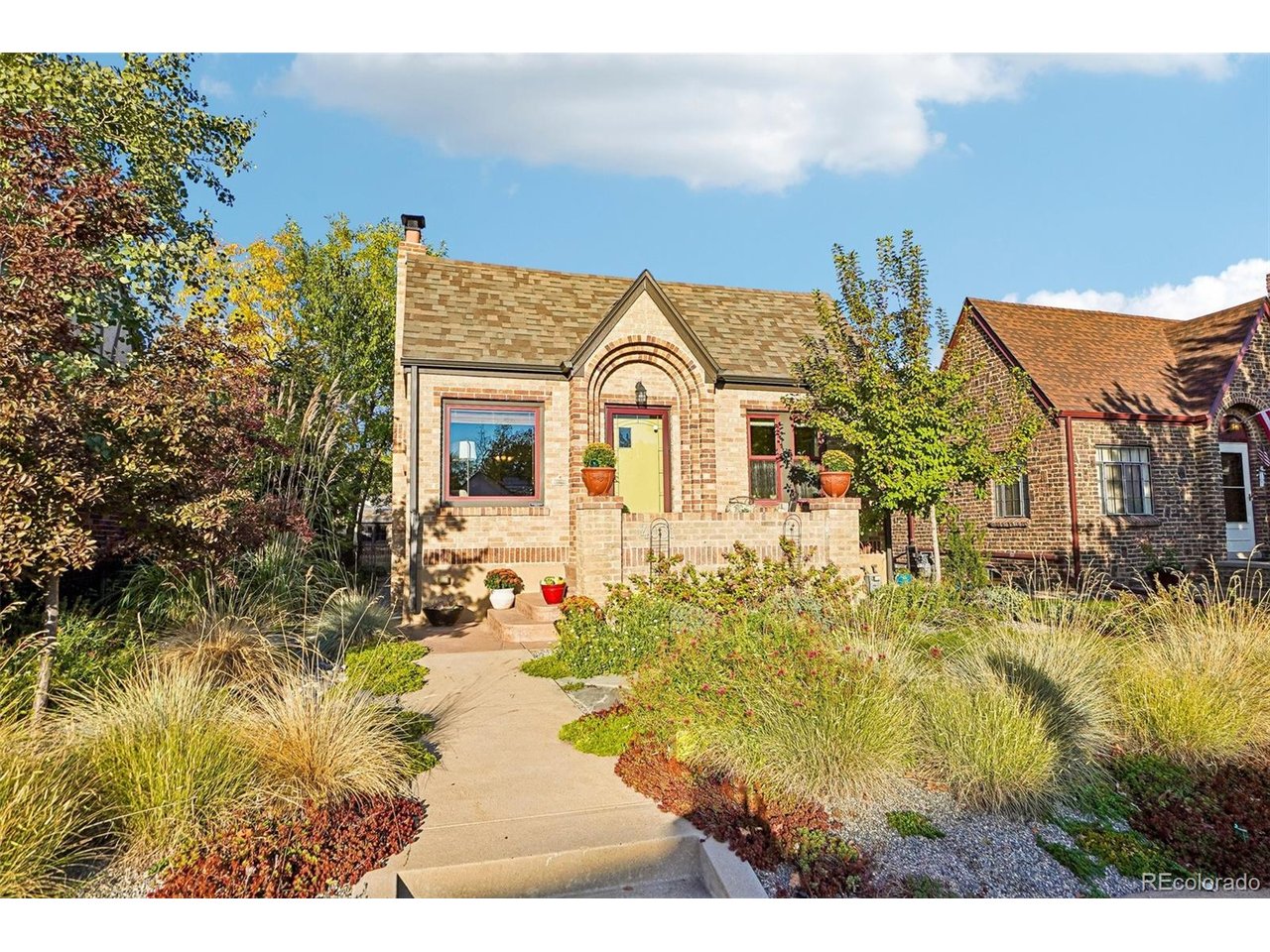 Brick house with an arched entry and yellow door, framed by mature landscaped gardens.