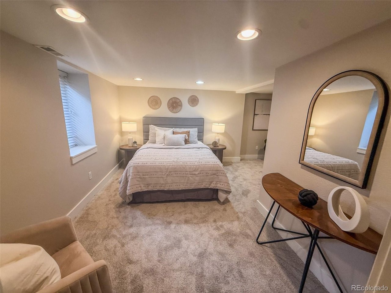 Furnished bedroom with a centered bed, bedside lamps, carpet, and an arched mirror above a console table.