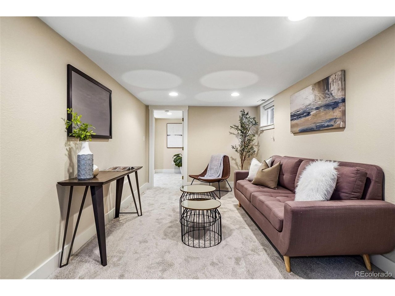 Staged basement living room with a mauve sofa and round nesting coffee tables.