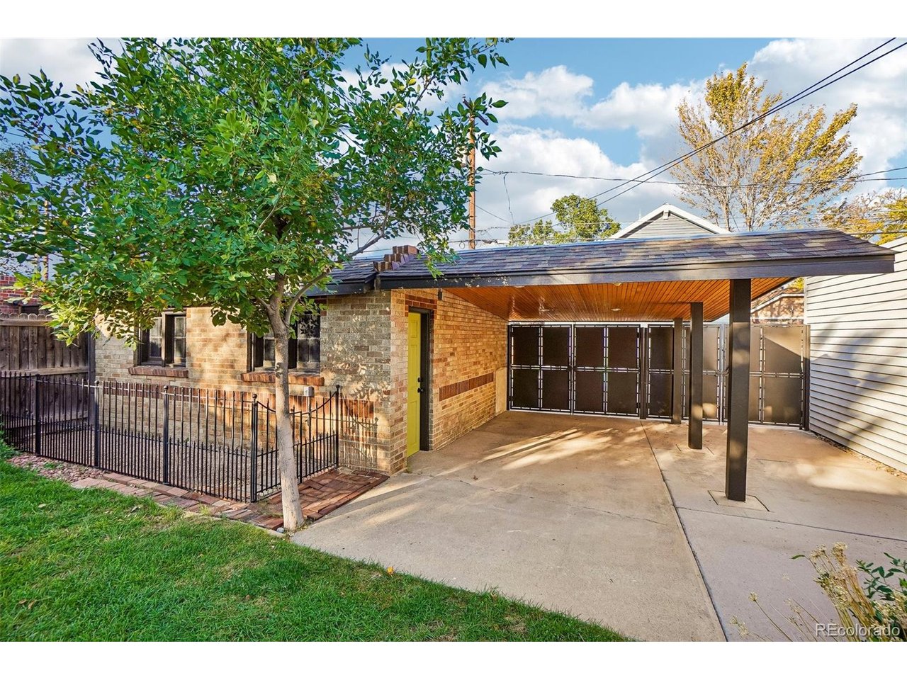 Brick home with a covered driveway, dark metal gate, and fenced front yard.