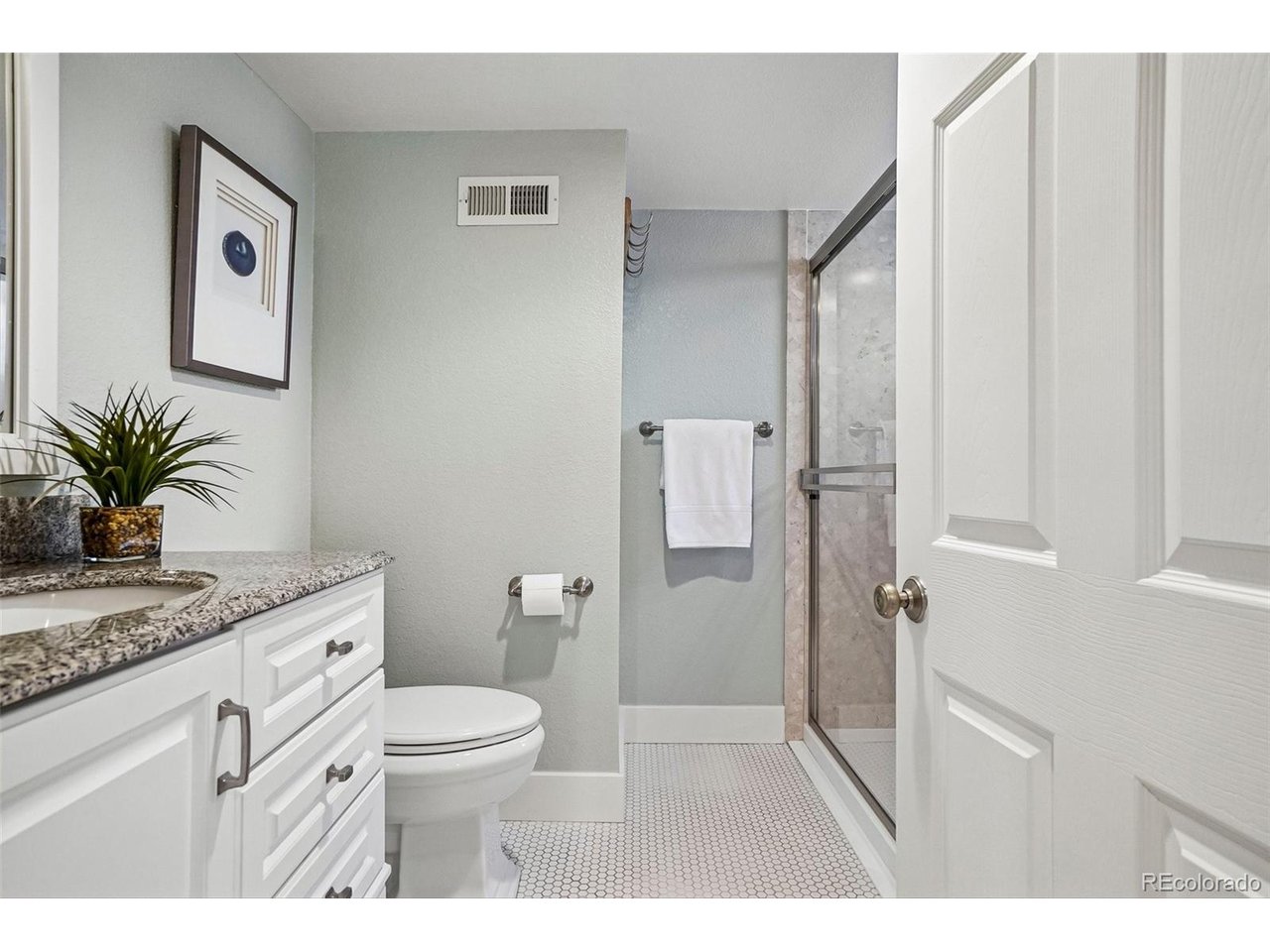 Bathroom with a granite vanity, small hexagonal floor tiles, and a glass-enclosed shower.
