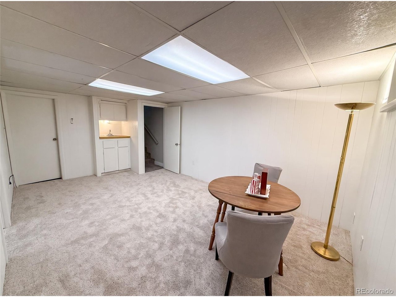 Carpeted lower-level sitting area with a small table, chairs, sink cabinet, and open stairway.