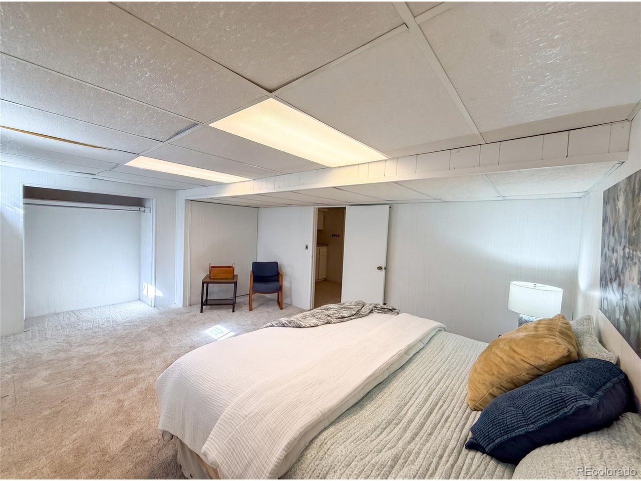 Bedroom with a low drop ceiling, beige carpet, and a bed with white and blue bedding.