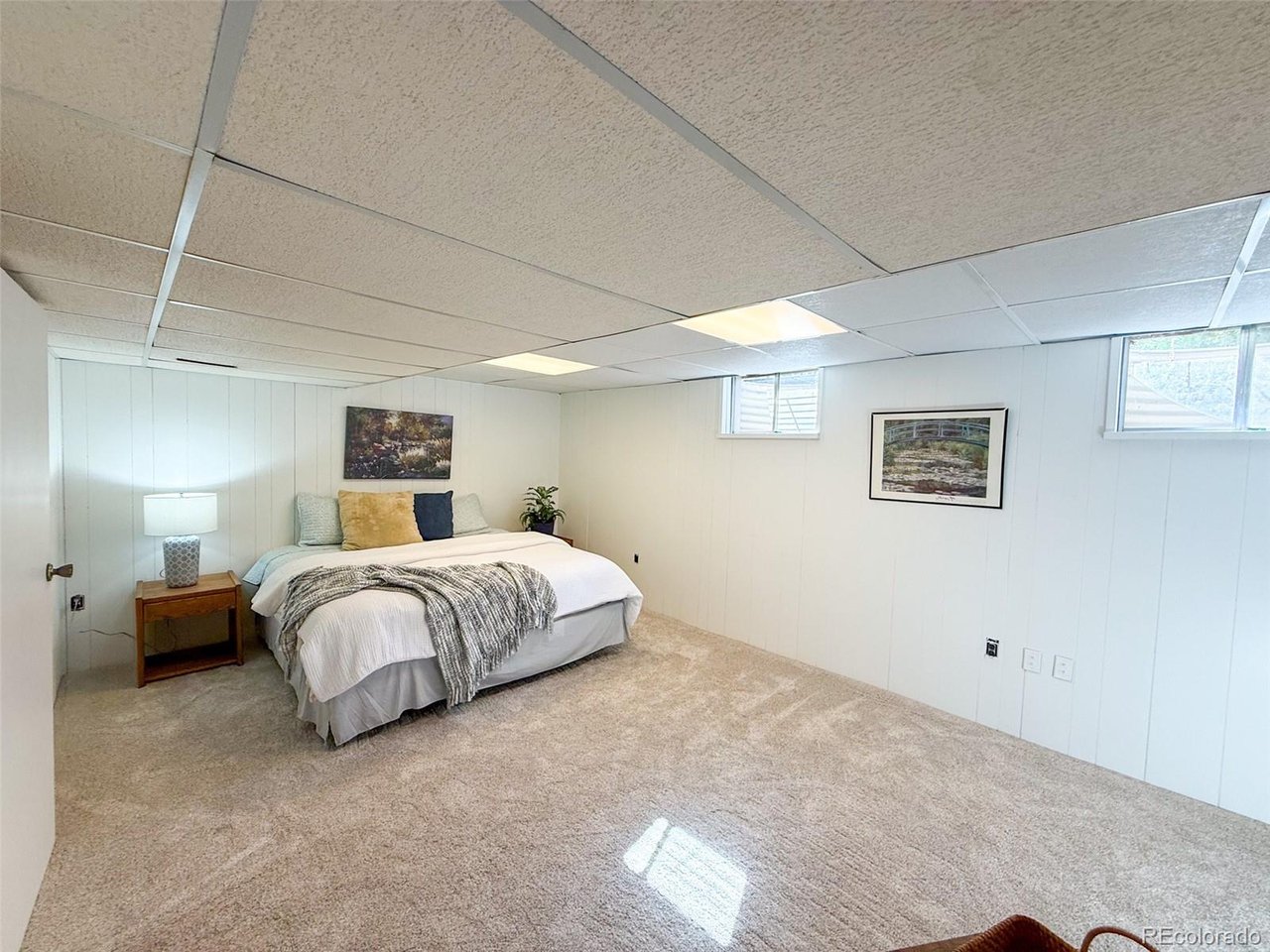 Furnished basement bedroom with a bed, beige carpet, and small high-set windows.