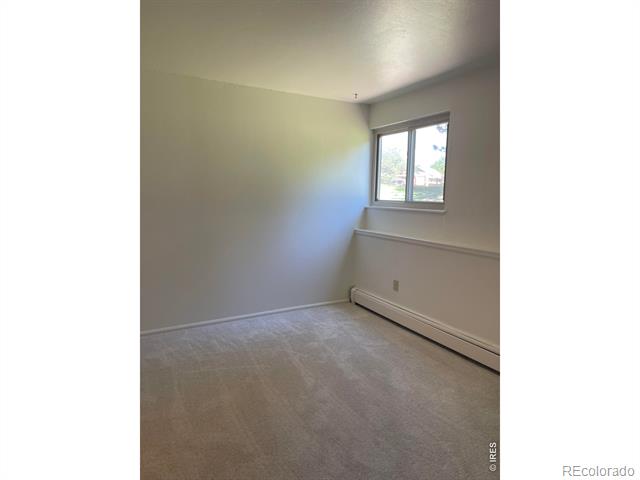 Vacant carpeted room with a single window and baseboard heater.
