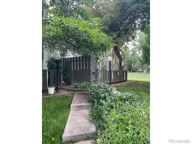 Landscaped courtyard with a concrete walkway leading to a dark fence beneath mature trees.