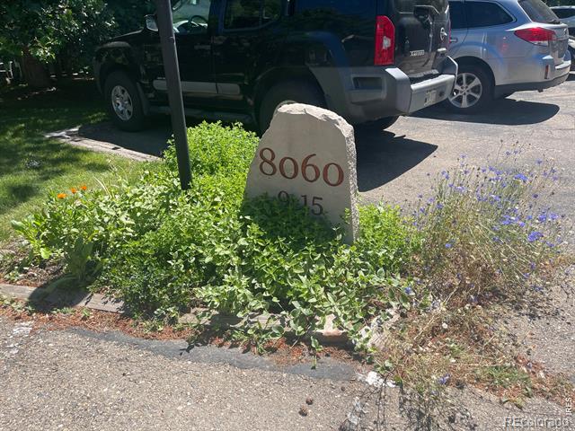 Stone 8060 address marker amid flowering landscaping beside a parking area.