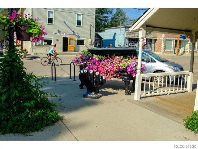 Sidewalk flower planters in front of storefronts, with a cyclist passing by.
