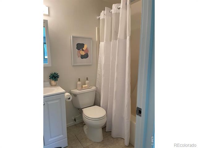 Bathroom with a white vanity and toilet beside a curtained shower.